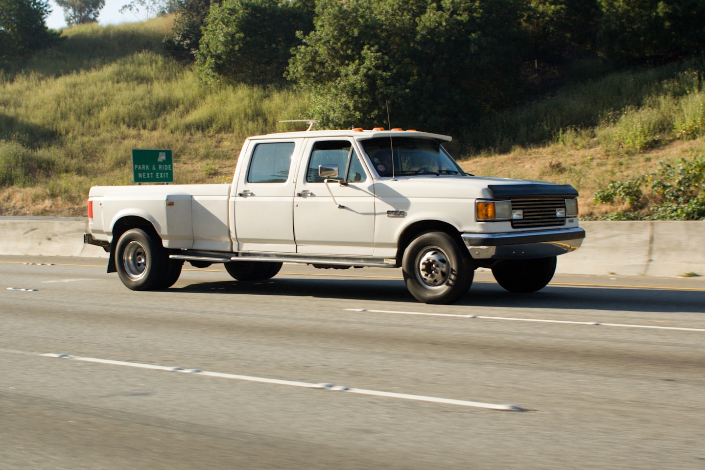 A white pickup truck driving along a highway hillside.