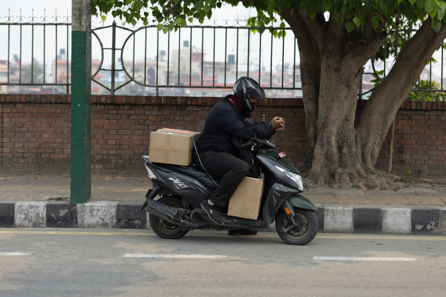 Delivery person on scooter with packages by brick wall.